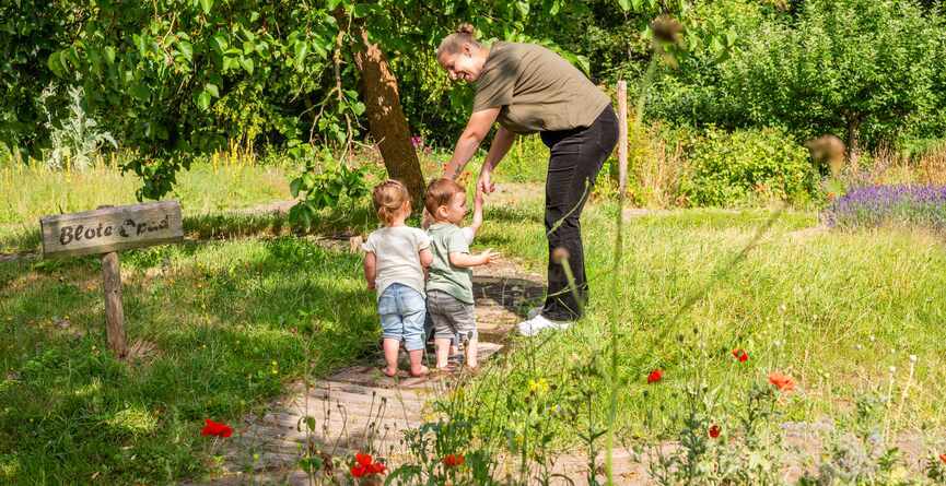 Vrouw neemt twee kinderen bij de hand op het blotevoetenpad