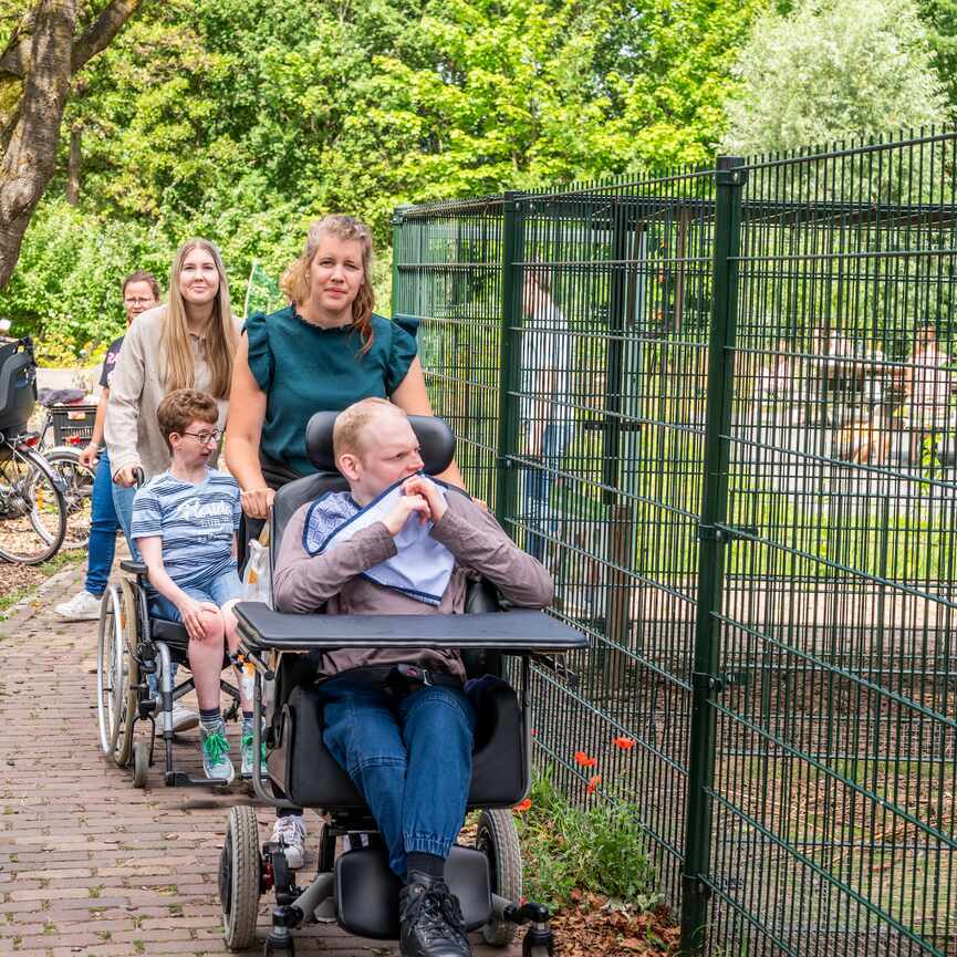 2 mensen in een rolstoel met hun begeleiders bij de dierenverblijven