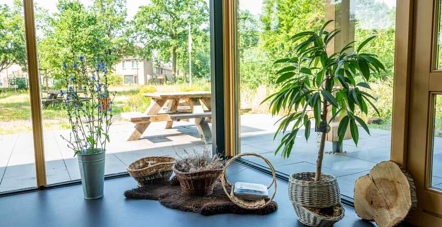 Manden en planten binnen. Picknicktafel buiten zien we door het glas